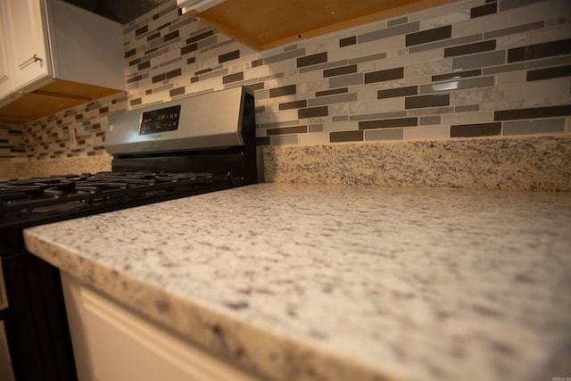 kitchen with gas stove, light stone counters, white cabinetry, and backsplash