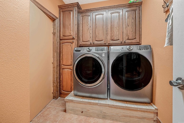 laundry room featuring washer and clothes dryer, cabinets, and light tile patterned floors