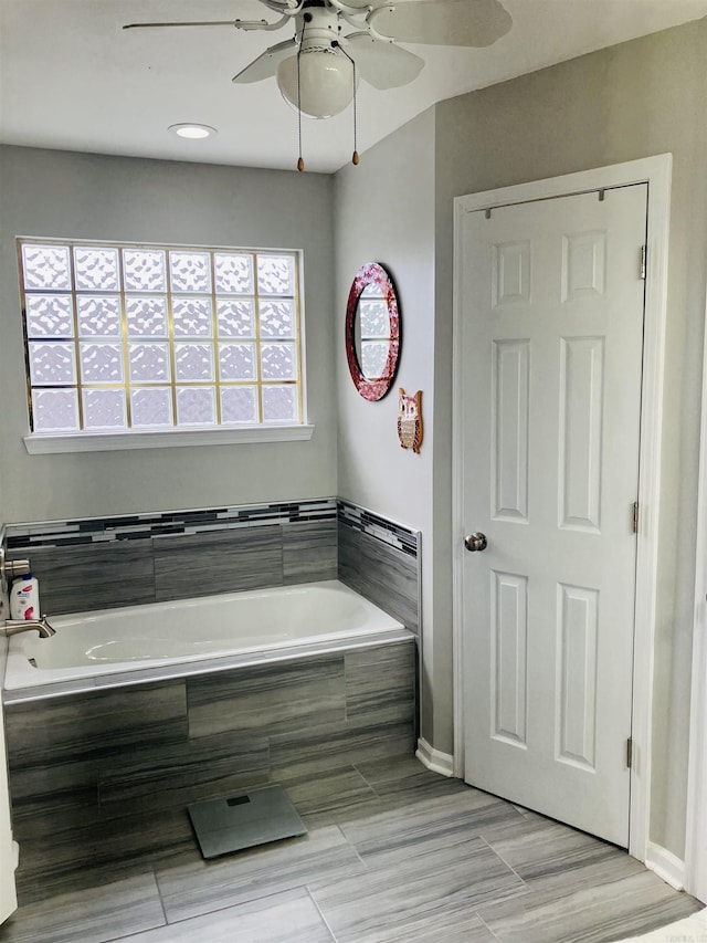 bathroom with tiled tub and ceiling fan