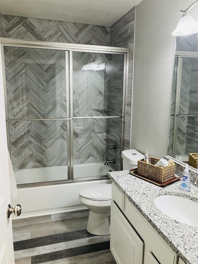 full bathroom with enclosed tub / shower combo, vanity, toilet, and wood-type flooring