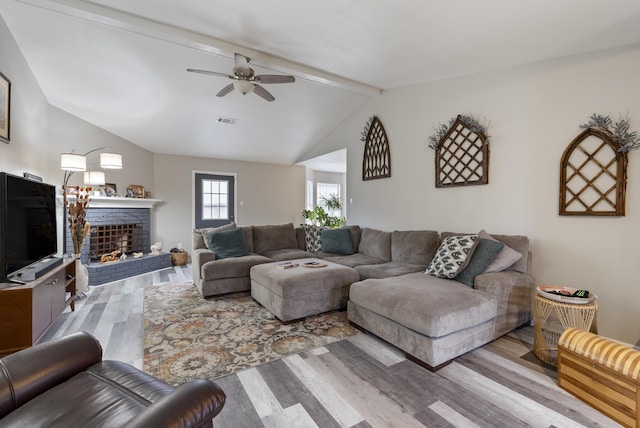 living room with ceiling fan, vaulted ceiling with beams, a fireplace, and light hardwood / wood-style flooring