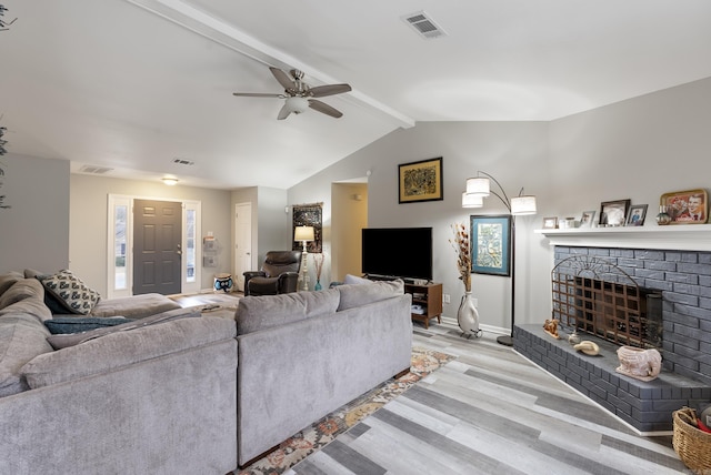 living room featuring lofted ceiling with beams, a brick fireplace, ceiling fan, and light hardwood / wood-style flooring