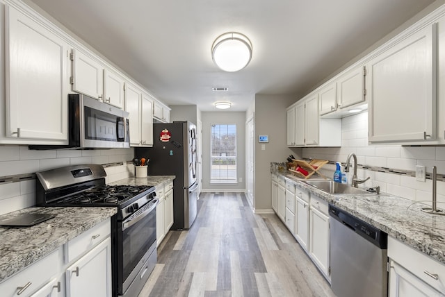 kitchen featuring sink, light stone counters, light hardwood / wood-style flooring, appliances with stainless steel finishes, and white cabinets