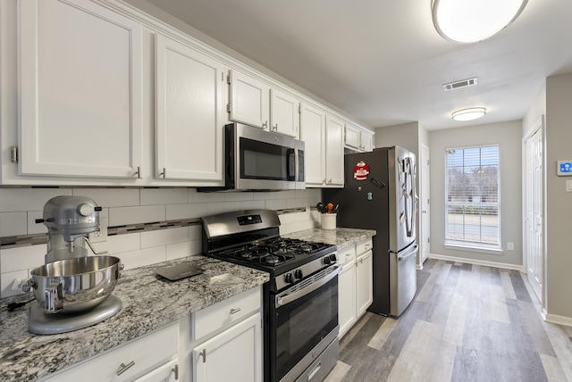 kitchen with white cabinetry, light stone counters, appliances with stainless steel finishes, light hardwood / wood-style floors, and decorative backsplash