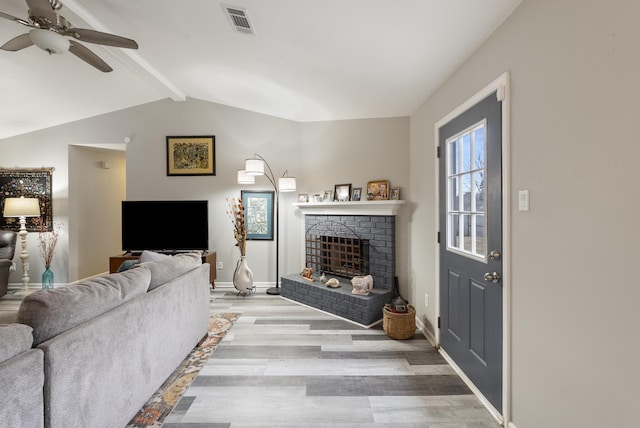 living room featuring ceiling fan, vaulted ceiling with beams, a fireplace, and light wood-type flooring