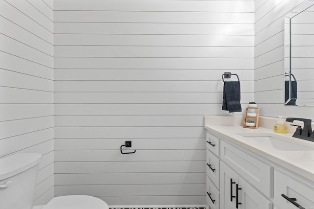 bathroom with vanity, toilet, and wood walls