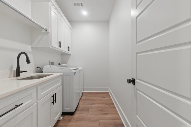 washroom with washing machine and clothes dryer, sink, cabinets, and light hardwood / wood-style flooring