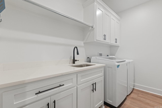 laundry area with washer and clothes dryer, sink, cabinets, and light wood-type flooring