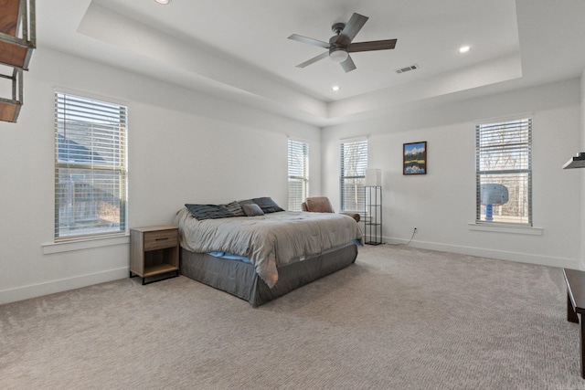 bedroom with light colored carpet, a raised ceiling, and ceiling fan