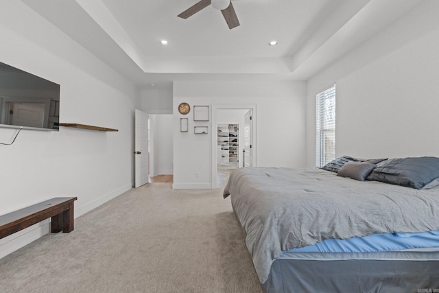 bedroom with light colored carpet, a raised ceiling, and ceiling fan