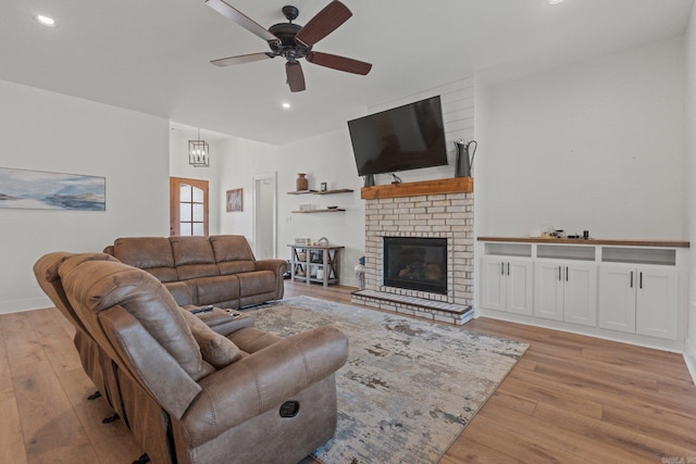 living room featuring ceiling fan with notable chandelier, light wood-type flooring, and a brick fireplace