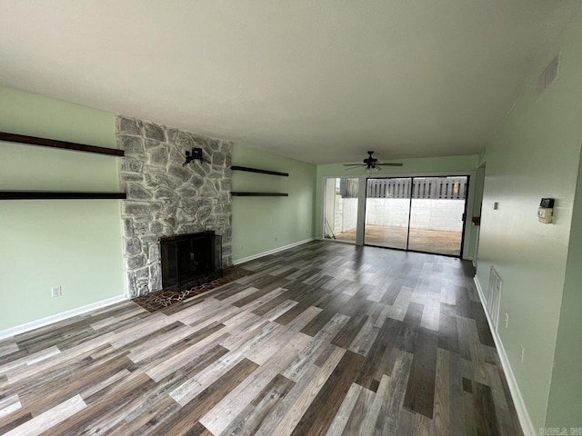 unfurnished living room featuring hardwood / wood-style flooring, ceiling fan, and a stone fireplace