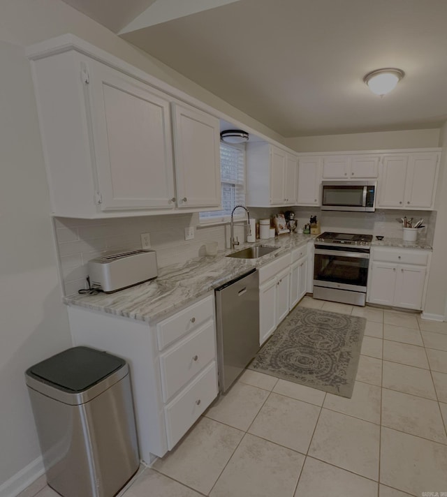 kitchen with appliances with stainless steel finishes, light stone counters, white cabinets, light tile patterned flooring, and sink