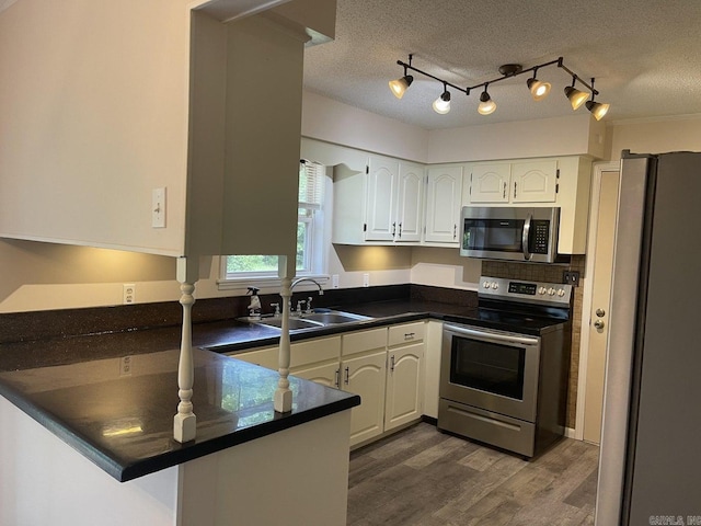 kitchen with white cabinets, kitchen peninsula, a textured ceiling, and appliances with stainless steel finishes