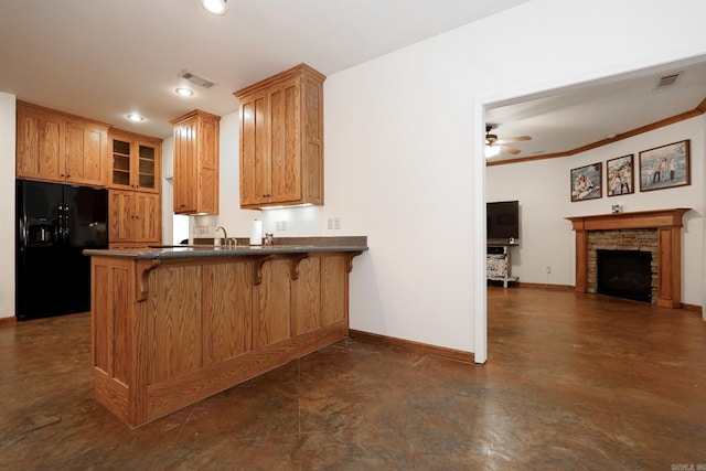 kitchen featuring ceiling fan, black fridge with ice dispenser, kitchen peninsula, a fireplace, and a breakfast bar