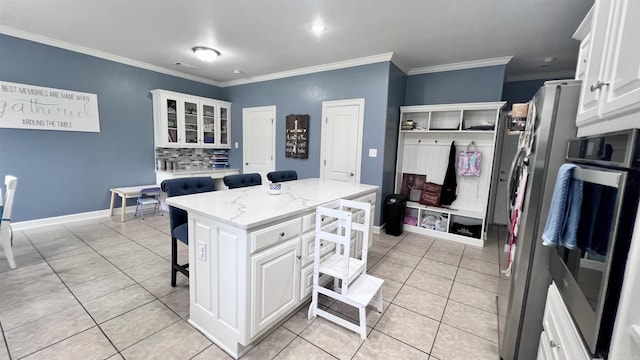 kitchen featuring a kitchen bar, a kitchen island, crown molding, light tile patterned floors, and white cabinetry