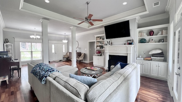 living room featuring dark wood-type flooring, ceiling fan with notable chandelier, a raised ceiling, crown molding, and built in shelves