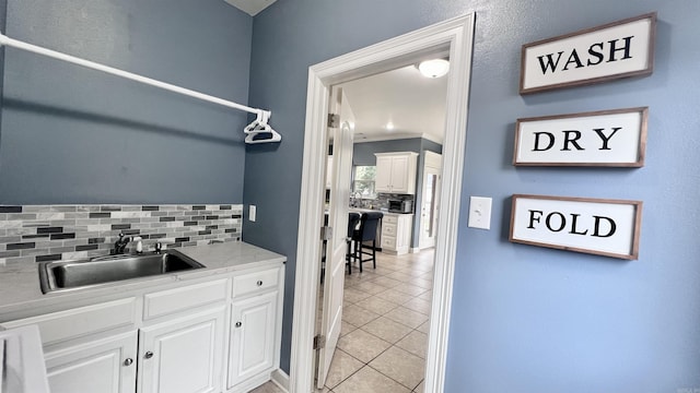 kitchen featuring sink, ornamental molding, light tile patterned floors, tasteful backsplash, and white cabinetry