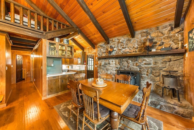 dining room with sink, beamed ceiling, light hardwood / wood-style floors, wooden walls, and wood ceiling