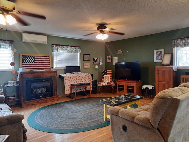 living room with a wall mounted AC, ceiling fan, hardwood / wood-style floors, and a textured ceiling