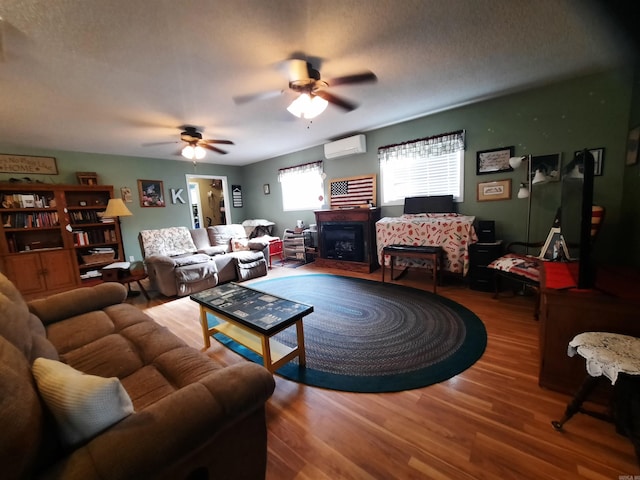 living room featuring hardwood / wood-style floors, ceiling fan, an AC wall unit, and a textured ceiling