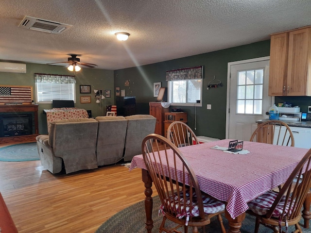 dining area with a wall mounted AC, ceiling fan, a textured ceiling, and light wood-type flooring