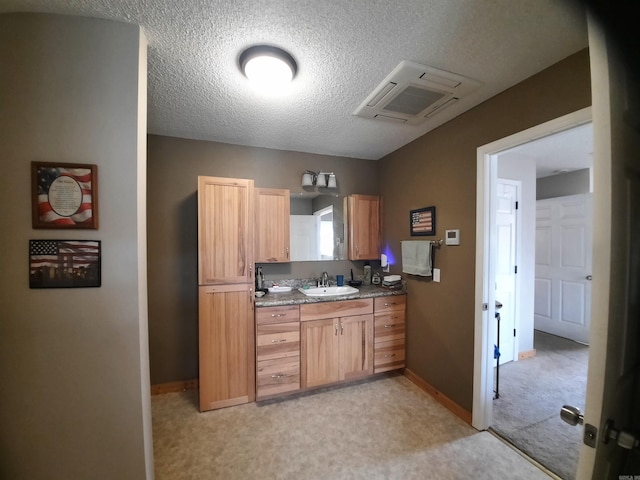 kitchen with light carpet, a textured ceiling, sink, light brown cabinets, and dark stone countertops