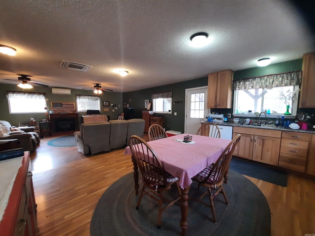 dining room featuring sink, ceiling fan, a textured ceiling, a fireplace, and wood-type flooring