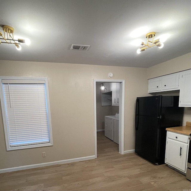 kitchen featuring white cabinetry, an inviting chandelier, light hardwood / wood-style flooring, black refrigerator, and washer and clothes dryer