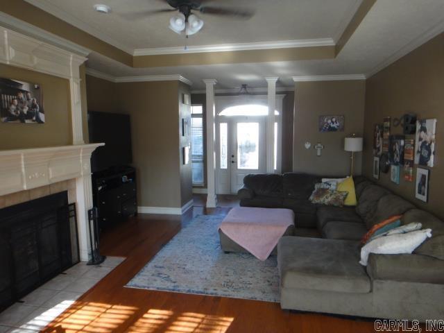 living room with a raised ceiling, a tiled fireplace, ceiling fan, and ornamental molding