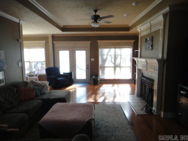 living room featuring a tray ceiling, ceiling fan, a fireplace, and ornamental molding