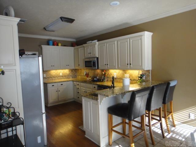 kitchen featuring kitchen peninsula, decorative backsplash, a kitchen bar, white cabinetry, and stainless steel appliances