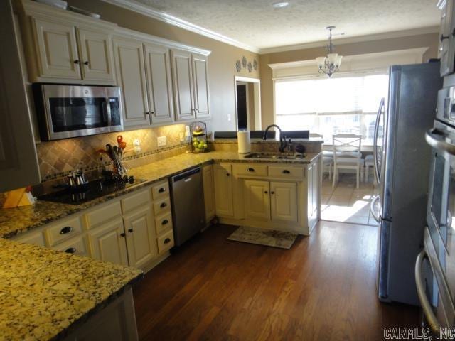 kitchen featuring sink, hanging light fixtures, kitchen peninsula, cream cabinets, and appliances with stainless steel finishes