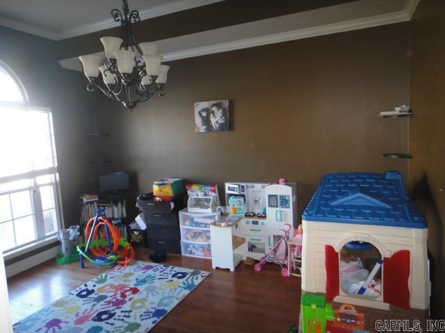 rec room with hardwood / wood-style flooring, crown molding, baseboard heating, and a chandelier