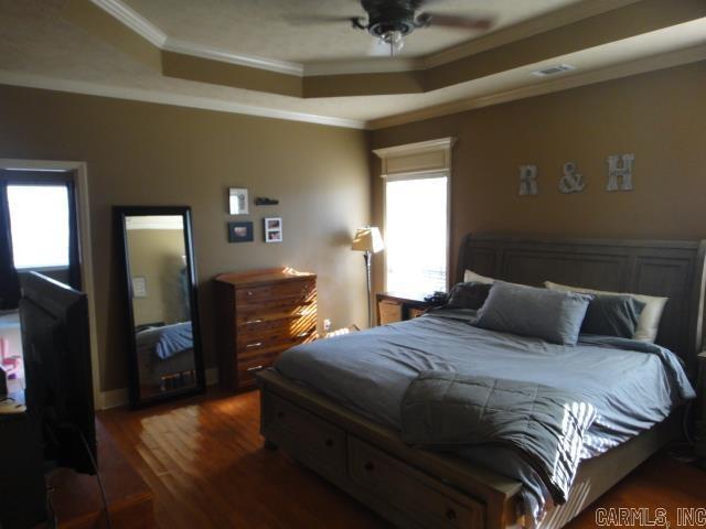 bedroom featuring dark hardwood / wood-style flooring, a raised ceiling, ceiling fan, and crown molding