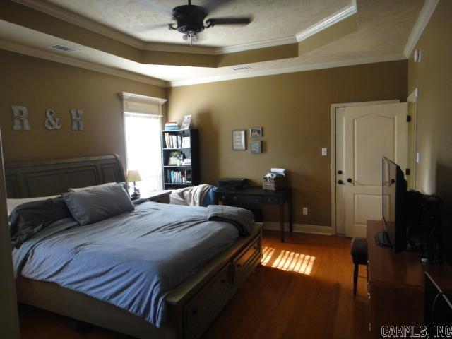 bedroom with hardwood / wood-style floors, ceiling fan, a raised ceiling, and ornamental molding