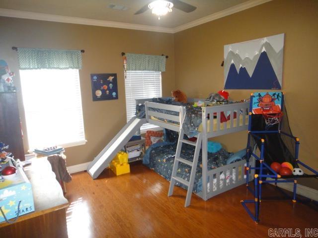 bedroom featuring multiple windows, wood-type flooring, ceiling fan, and ornamental molding