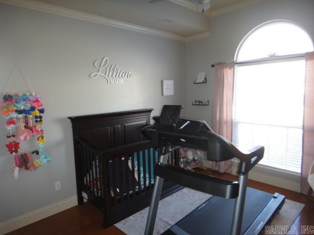 bedroom with wood-type flooring, a nursery area, and crown molding