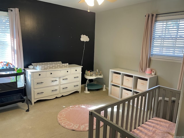 carpeted bedroom with ceiling fan and a nursery area