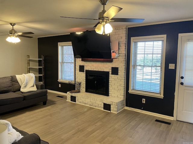 living room with ceiling fan, ornamental molding, wood-type flooring, and a brick fireplace