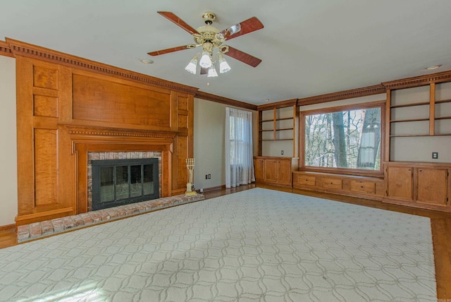 unfurnished living room with a fireplace, built in shelves, ceiling fan, and crown molding