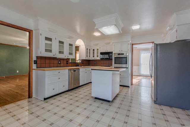 kitchen featuring tasteful backsplash, ornamental molding, stainless steel appliances, a kitchen island, and white cabinetry