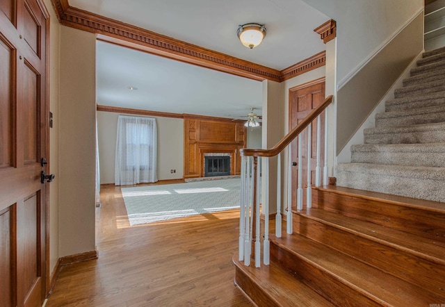 foyer entrance with light wood-type flooring, a large fireplace, ceiling fan, and ornamental molding