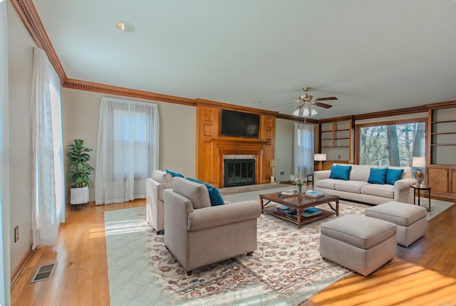 living room featuring ceiling fan, light wood-type flooring, ornamental molding, and built in shelves