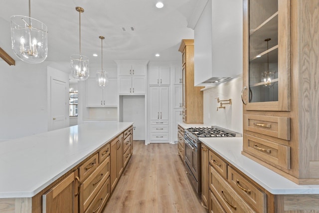 kitchen featuring wall chimney exhaust hood, decorative light fixtures, range with two ovens, a center island, and white cabinetry