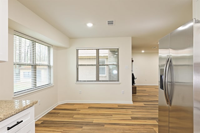 kitchen featuring stainless steel refrigerator with ice dispenser, light hardwood / wood-style floors, white cabinetry, and light stone counters