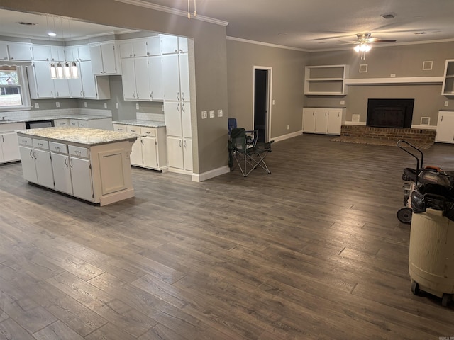 kitchen featuring ceiling fan, crown molding, a fireplace, a center island, and white cabinetry