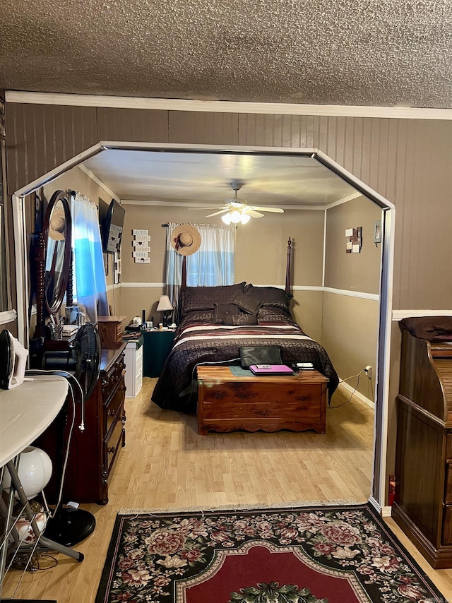 bedroom with ceiling fan, light wood-type flooring, wood walls, and ornamental molding