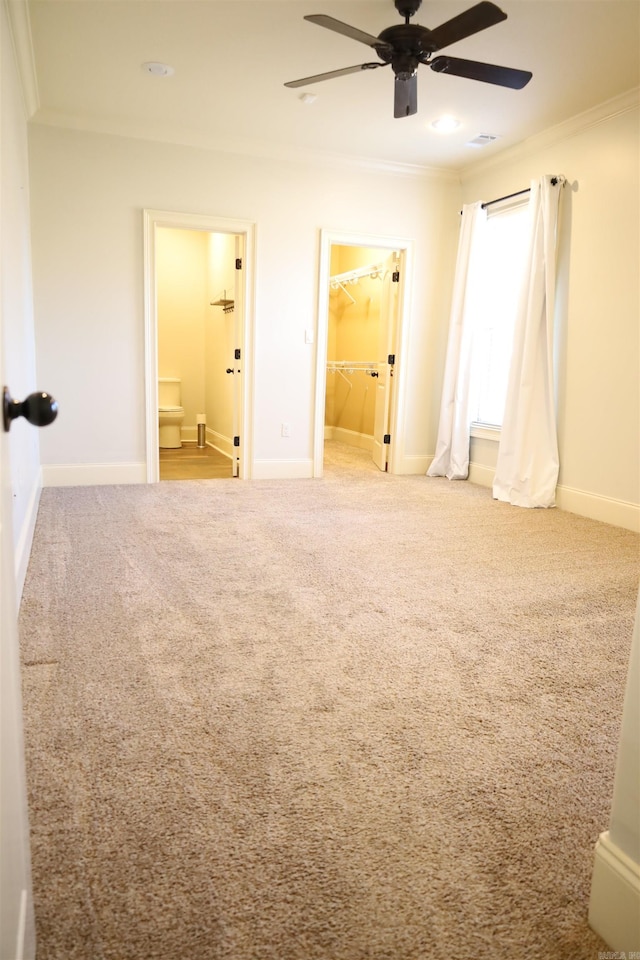 unfurnished bedroom featuring carpet flooring, a spacious closet, crown molding, and ceiling fan