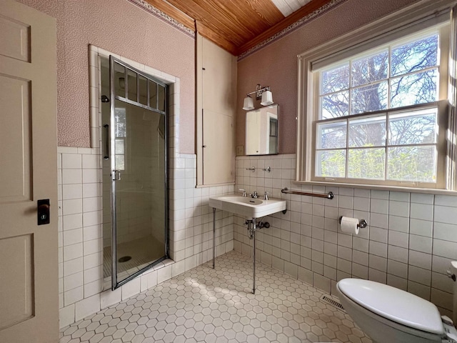 bathroom featuring wooden ceiling, crown molding, toilet, a shower with door, and tile walls